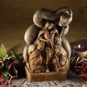 May include: A wooden statue of the Norse goddess Freya, depicted with a wolf and a serpent. The statue is carved with intricate details and features the rune for Freya, "F", on the base.