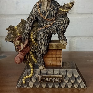 May include: A Krampus figurine with a horned head, shaggy fur, and a gold chain. The figure is perched on a chimney, holding a sack and a string of beads. The base is inscribed with the name "Krampus".