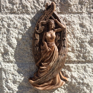 May include: A wooden carving of a winged woman with flowing hair and a long dress. The carving is detailed and intricate, with the woman's wings and dress flowing in the wind.