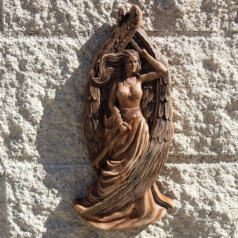 May include: A wooden carving of a winged woman with flowing hair and a long dress. The carving is detailed and intricate, with the woman's wings and dress flowing in the wind.