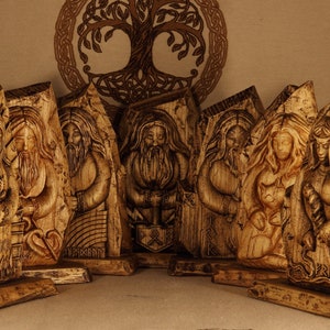 May include: A set of eight wooden carvings depicting Norse gods and goddesses. The carvings are detailed and intricate, with each figure standing on a wooden base. The carvings are painted in shades of brown and gold.
