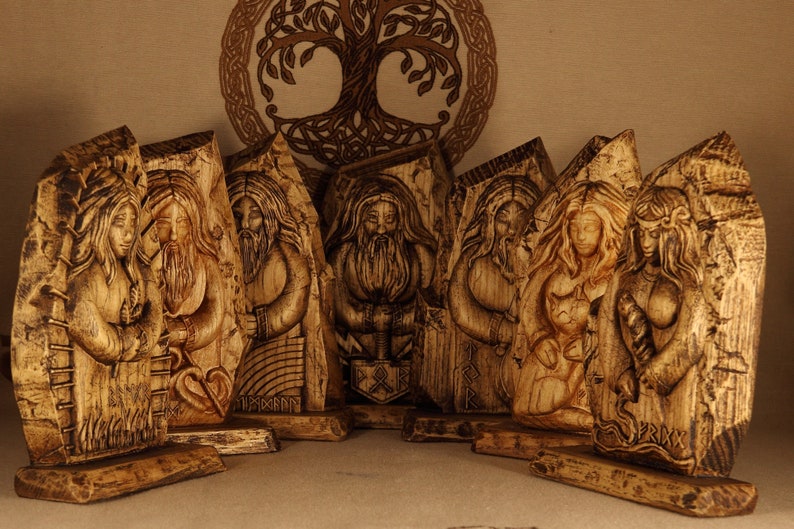 May include: A set of eight wooden carvings depicting Norse gods and goddesses. The carvings are detailed and intricate, with each figure standing on a wooden base. The carvings are painted in shades of brown and gold.