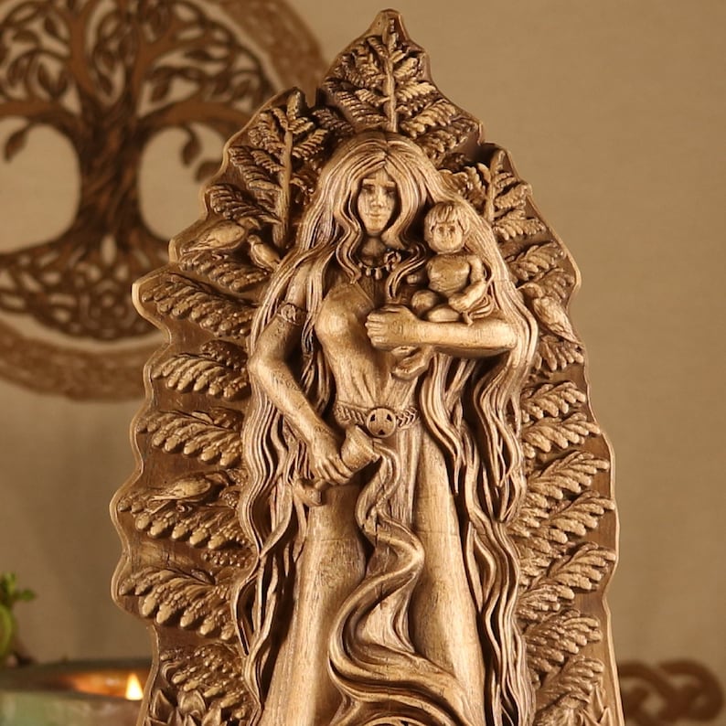 May include: A wooden carving of a woman holding a child, surrounded by intricate foliage. The woman is wearing a long dress and has long flowing hair. The carving is a representation of the Norse goddess Freya.