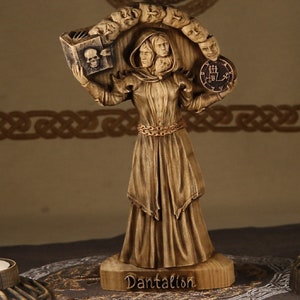 Puede incluir: Estatua de madera de un demonio con múltiples caras, sosteniendo un libro y un sello. La estatua está de pie sobre una base de madera con el nombre "Dantalion" inscrito en ella.
