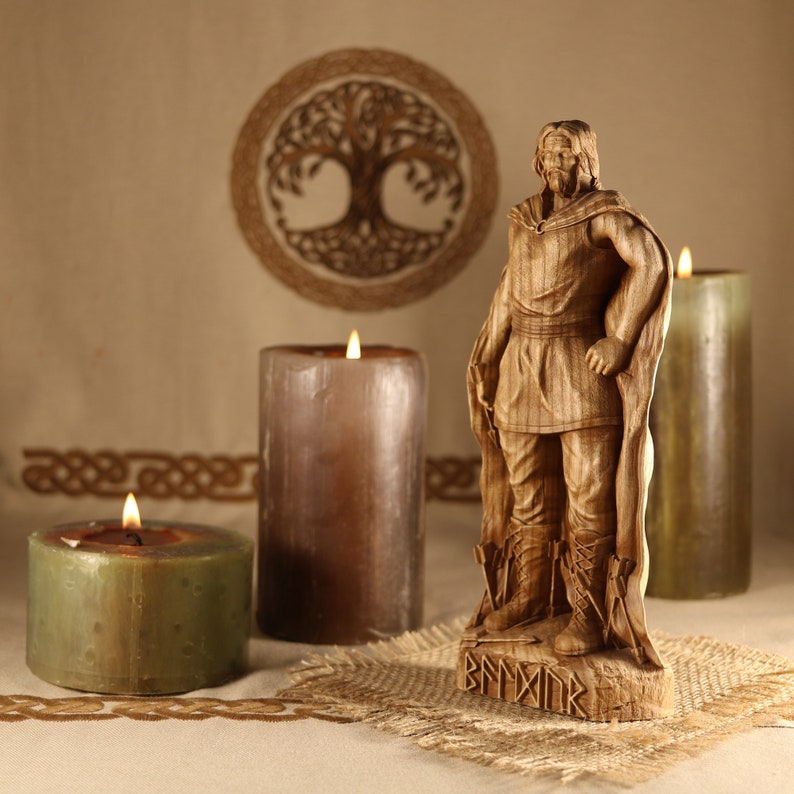 May include: A wooden carving of a Viking warrior standing on a base with runes. The warrior is wearing a cloak and holding a sword. The carving is surrounded by three candles.