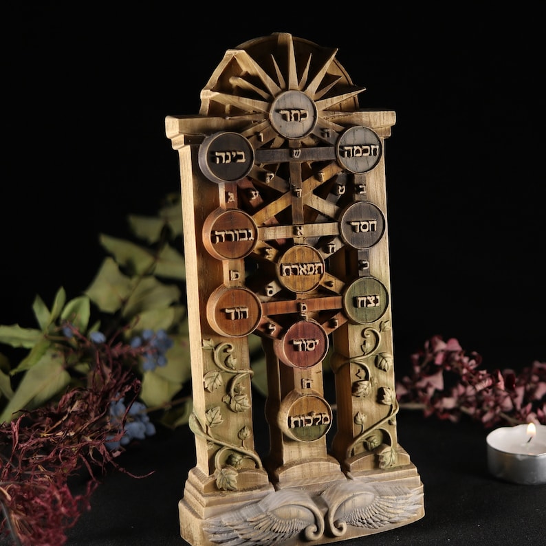 May include: A wooden Tree of Life sculpture with Hebrew text, featuring a central trunk with branches extending to ten circular leaves, each with a different Hebrew word. The sculpture is carved with intricate details, including a sunburst at the top and wings at the base.
