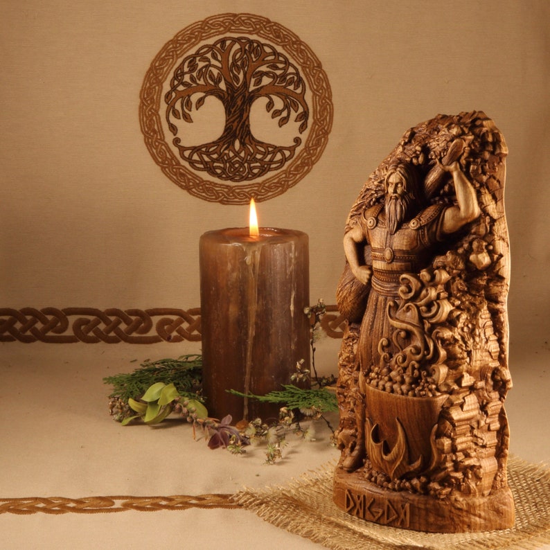 K&ouml;nnte beinhalten: Handgeschnitzte Holzstatue eines nordischen Gottes, m&ouml;glicherweise Thor, der einen Hammer h&auml;lt. Die Statue steht auf einem Holzsockel mit der Inschrift "DAGAZ". Die Statue ist von einem geschnitzten Baum und einer Kerze umgeben.