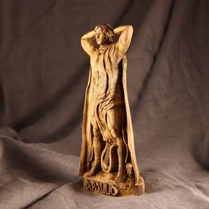 K&ouml;nnte beinhalten: Eine Holzskulptur des griechischen Gottes Apollon, der mit erhobenen Armen &uuml;ber dem Kopf steht. Die Skulptur ist realistisch gearbeitet und weist komplizierte Details auf. Der Sockel der Skulptur ist mit dem Wort "APOLLO" beschriftet.