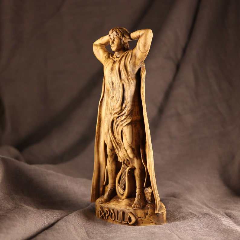 K&ouml;nnte beinhalten: Eine Holzskulptur des griechischen Gottes Apollon, der mit erhobenen Armen &uuml;ber dem Kopf steht. Die Skulptur ist realistisch gearbeitet und weist komplizierte Details auf. Der Sockel der Skulptur ist mit dem Wort "APOLLO" beschriftet.