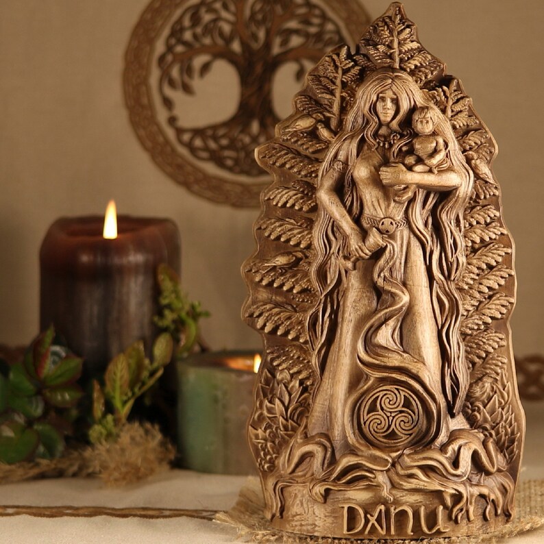 May include: A wooden carving of the Celtic goddess Danu, holding a child. The carving is detailed and intricate, with a tree of life design in the background. The carving is labeled "Danu" at the bottom.