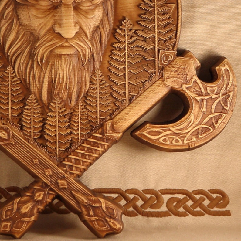 May include: A wooden wall hanging featuring a carved image of a bearded man's face surrounded by trees and ferns. Two crossed axes with intricate carvings are below the face.