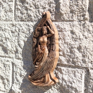 May include: A wooden carving of a winged figure with long flowing hair and a flowing gown. The figure is holding a sword in one hand and has a crown on their head.