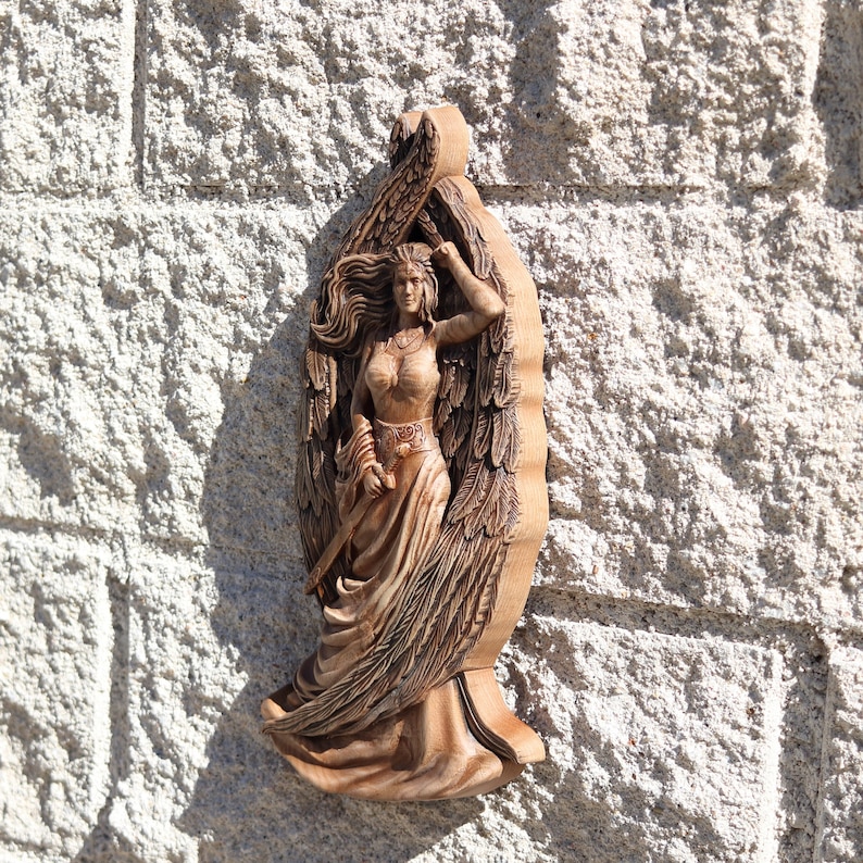 May include: A wooden carving of a winged figure with long flowing hair and a flowing gown. The figure is holding a sword in one hand and has a crown on their head.