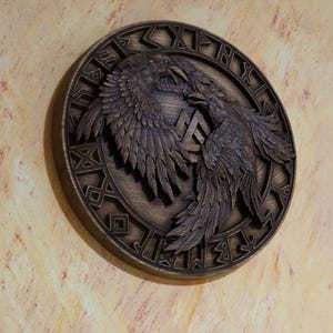 May include: A wooden wall plaque featuring a carved design of two ravens flanking a Vegvisir symbol. The ravens are intricately detailed with feathers and the Vegvisir is surrounded by a circle of runes.