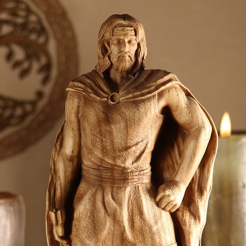 May include: A wooden sculpture of a person wearing a cloak and a crown. The sculpture is carved in a realistic style and has a warm brown color.