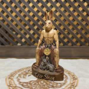 May include: A wooden statue of a rabbit-like deity, Tuer Shen, sitting on a throne with two smaller rabbits at his feet. The statue is painted in shades of brown and gold, with a red and gold robe.