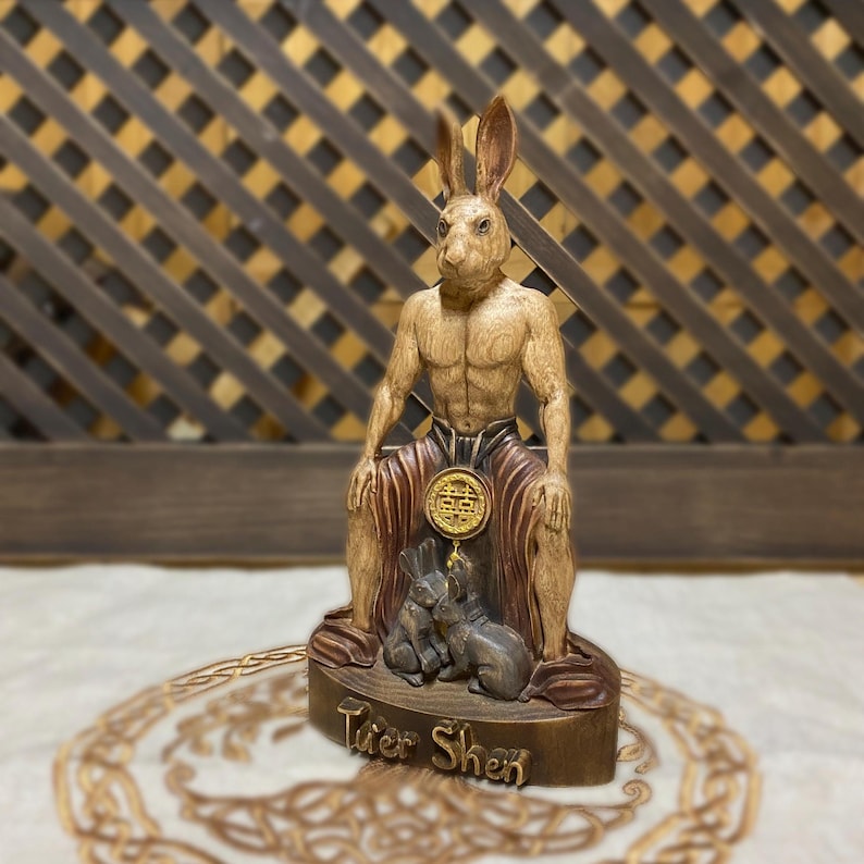 May include: A wooden statue of a rabbit-like deity, Tuer Shen, sitting on a throne with two smaller rabbits at his feet. The statue is painted in shades of brown and gold, with a red and gold robe.