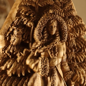 May include: A wooden sculpture of a woman with a detailed, intricate design. The woman is wearing a long, flowing robe and has a crown of leaves on her head. The sculpture is carved in a realistic style and has a warm, natural color.