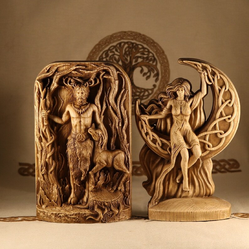 May include: Two wooden carvings, one depicting a horned figure with a deer, the other a woman holding a crescent moon.