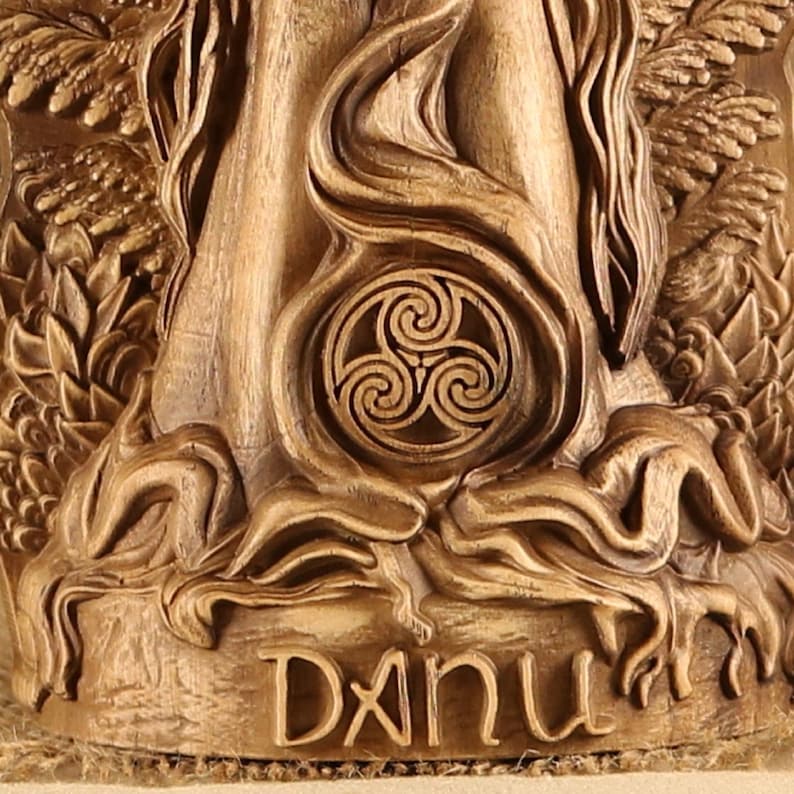 May include: A wooden carving of the Celtic goddess Danu, with a triple spiral symbol and the name "Danu" inscribed below. The carving is in a warm brown color and has a detailed, intricate design.