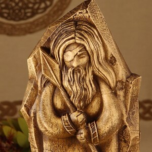 May include: A wooden sculpture of a bearded figure with a blindfold, holding a spear. The sculpture is carved in a detailed style, with intricate details in the hair, beard, and clothing.