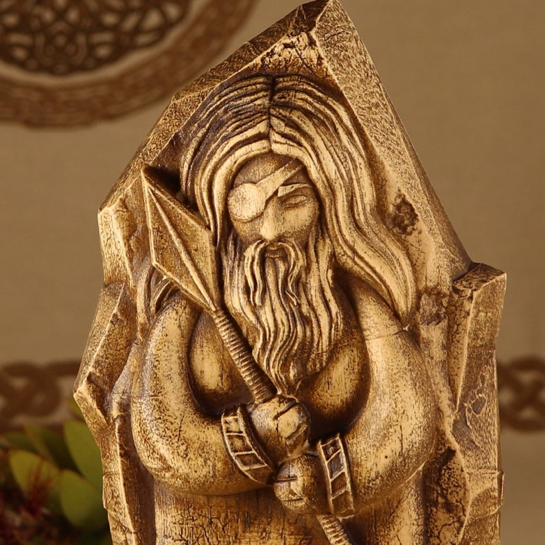 May include: A wooden sculpture of a bearded figure with a blindfold, holding a spear. The sculpture is carved in a detailed style, with intricate details in the hair, beard, and clothing.