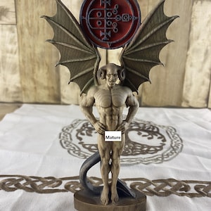 Può includere: Scultura in legno dettagliata di una figura demoniaca con ali da pipistrello, corna e una coda. La figura è in piedi su una base, con un emblema circolare rosso sopra la sua testa. La scultura ha un fisico muscoloso e un'espressione sinistra.