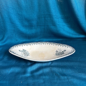 May include: An oval-shaped ceramic dish with a cream-coloured centre and a dark green decorative border featuring a repeating geometric pattern and floral motifs on the left and right sides of the interior basin.
