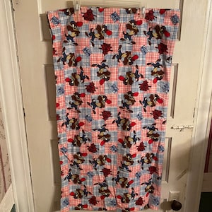 May include: A red, blue, and white checkered fabric blanket with a cartoon coyote design. The coyote is wearing a red bandana and is running.