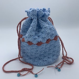 Puede incluir: Un bolso de ganchillo azul claro con un borde marr&oacute;n festoneado. El bolso tiene un patr&oacute;n texturizado y cordones marrones con cuentas azules. El bolso est&aacute; hecho a mano y es adecuado para llevar objetos peque&ntilde;os.