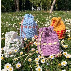 Puede incluir: Cuatro bolsas de crochet con cord&oacute;n hechas a mano en blanco, azul claro, morado y amarillo. Cada bolsa presenta un patr&oacute;n de puntadas texturizado y un acento de color contrastante cerca de la parte superior. Las bolsas est&aacute;n en un campo de margaritas.
