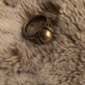 May include: A gold ring with a round, smooth top and intricate detailing on the band.