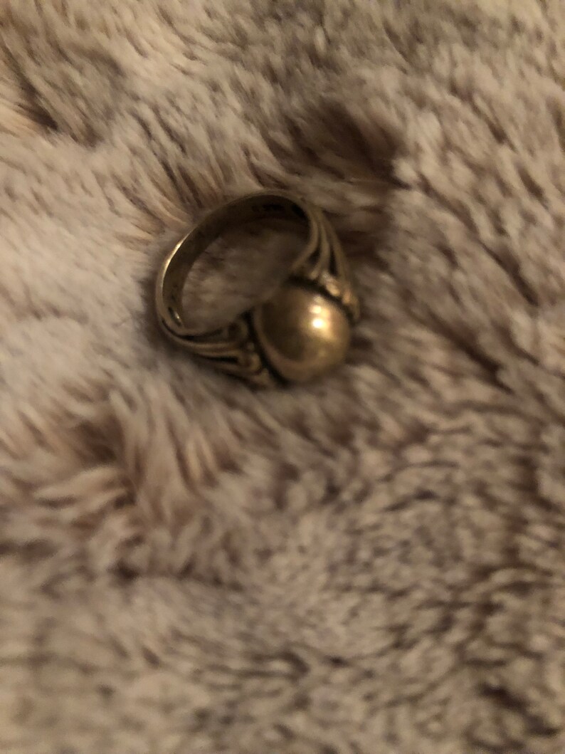 May include: A gold ring with a round, smooth top and intricate detailing on the band.