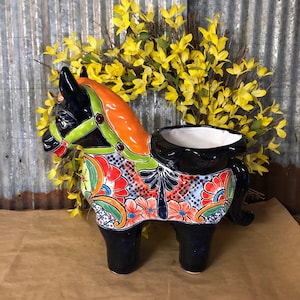 May include: A black ceramic horse planter with colorful floral designs. The planter has a green, orange, and red saddle and a white interior.