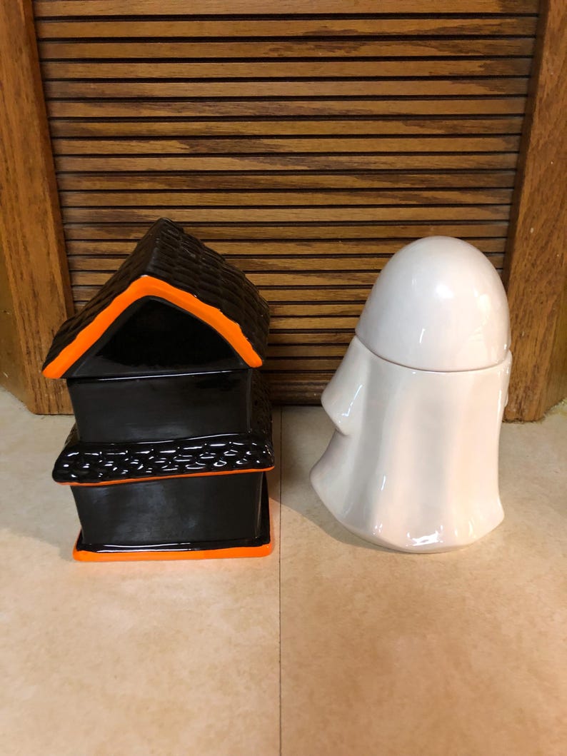 May include: Two Halloween themed ceramic containers. One is a black house with orange trim and the other is a white ghost.