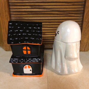 May include: A black and orange ceramic haunted house and a white ceramic ghost figurine. Both are Halloween themed decorations.