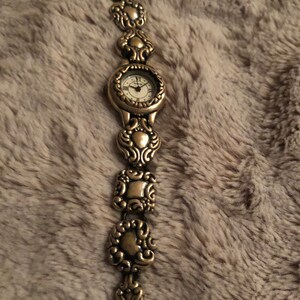 May include: A silver watch with a white face and ornate silver band. The band is made up of a series of linked, decorative, heart-shaped pieces.