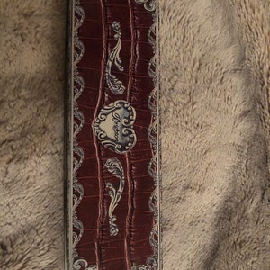 May include: A rectangular, red, faux leather box with a silver, ornate design. The box has a heart-shaped emblem with the word "Brighton" in white lettering.