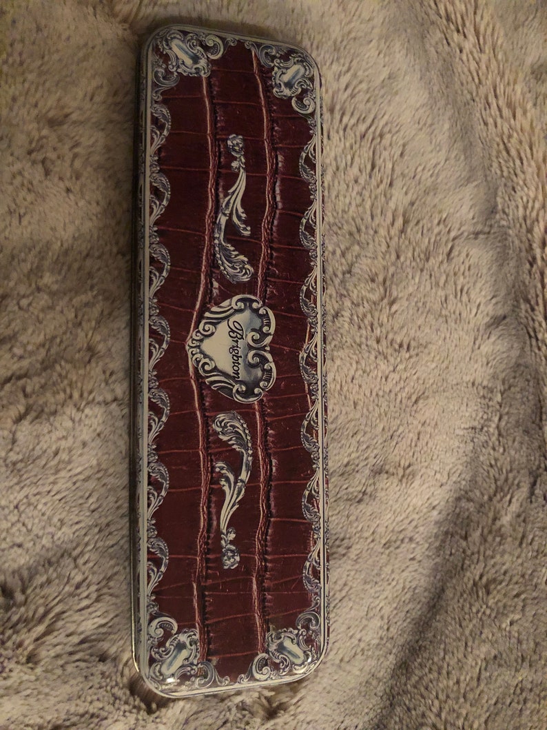 May include: A rectangular, red, faux leather box with a silver, ornate design. The box has a heart-shaped emblem with the word "Brighton" in white lettering.