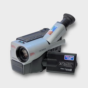 Peut inclure: Caméscope Samsung argenté et noir avec viseur noir et bloc-batterie noir. Le caméscope porte l'inscription "320x" et "COLOR LCD" sur le bloc-batterie.