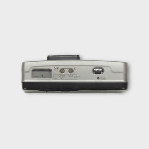 May include: Silver and black point-and-shoot camera. The camera has a small LCD screen and buttons labelled "AUTO", "MODE/SEL", "ADJ", and "DATE". The camera also has an "ON" button and a flash symbol.