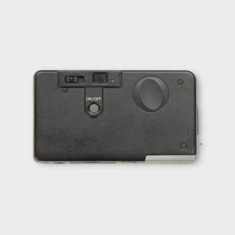 May include: A black rectangular camera with a flash and an on/off button. The camera has a small lens and a film advance wheel. The camera is a vintage model.