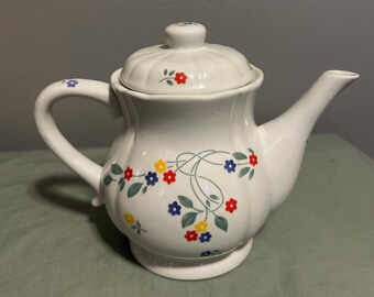 May include: White ceramic teapot with a floral design featuring red, yellow, and blue flowers. The teapot has a lid and a handle.
