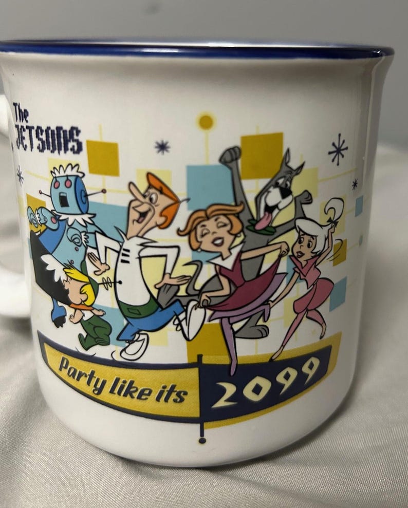 May include: White ceramic mug featuring a colorful illustration of The Jetsons cartoon characters. The mug has a blue rim and the text "Party like its 2099". The Jetsons characters are depicted in a retro style, with vibrant colors and dynamic poses.