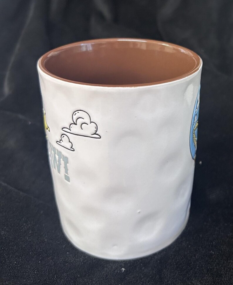 Pu&ograve; includere: Tazza in ceramica bianca con esterno strutturato e interno marrone. La tazza presenta grafiche di cartoni animati e la parola "WANT" in lettere grigie. La tazza &egrave; cilindrica e misura circa 10 cm di altezza.