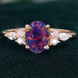 May include: A rose gold ring featuring an oval-cut, iridescent opal gemstone with a deep purple hue, accented by small, round, and pear-shaped white gemstones. The ring's band is a delicate, polished metal.
