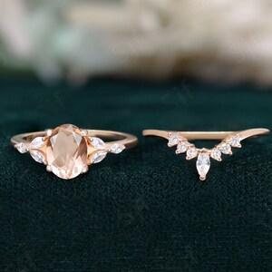 May include: A rose gold engagement ring set with an oval-shaped peach morganite center stone and a matching rose gold wedding band with marquise-shaped diamonds.