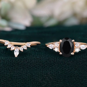 May include: A rose gold engagement ring with a black oval gemstone and a matching rose gold wedding band with a row of marquise-shaped diamonds.