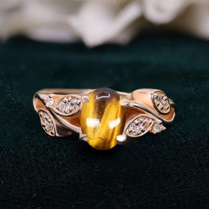 May include: A gold ring with a large oval tiger's eye gemstone surrounded by smaller clear gemstones set in a leaf design.