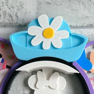 May include: A light blue headband with a white daisy flower and a white bow. The headband is made of foam and is designed to look like a hat.